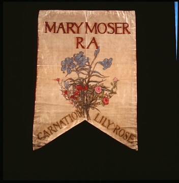 A decorative banner featuring the name Mary Moser with R A beneath it. Below the text, there is an artistic depiction of a floral arrangement featuring blue, pink, and red flowers. The banner has a pointed end with the words 'Carnation Lily Rose' at the bottom.