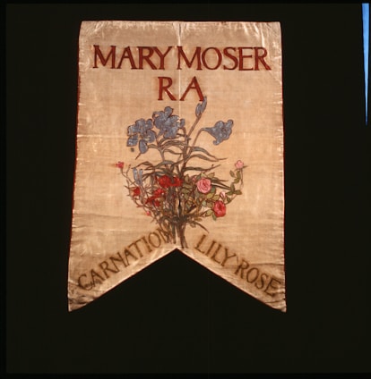 A decorative banner featuring the name Mary Moser with R A beneath it. Below the text, there is an artistic depiction of a floral arrangement featuring blue, pink, and red flowers. The banner has a pointed end with the words 'Carnation Lily Rose' at the bottom.