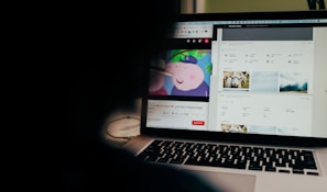 A partially obscured view of a laptop screen displaying two separate browser tabs. The left tab shows a children's cartoon video, while the right tab appears to be a webpage with photos and metadata, possibly related to stock photography. The foreground is dark, highlighting the screen's content.