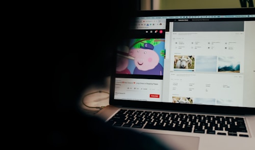 A partially obscured view of a laptop screen displaying two separate browser tabs. The left tab shows a children's cartoon video, while the right tab appears to be a webpage with photos and metadata, possibly related to stock photography. The foreground is dark, highlighting the screen's content.
