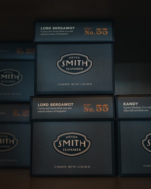 Several stacked boxes of Steven Smith Teamaker tea, labeled with the blend 'Lord Bergamot' and 'Kandy'. The packaging is dark with orange and white text, highlighting blend numbers 55 and 23.