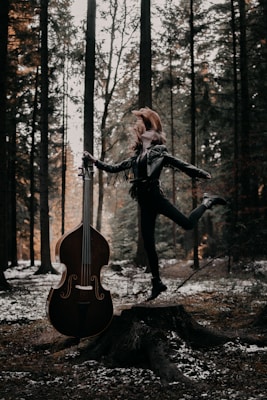woman in black jacket and black pants playing violin in forest during daytime
