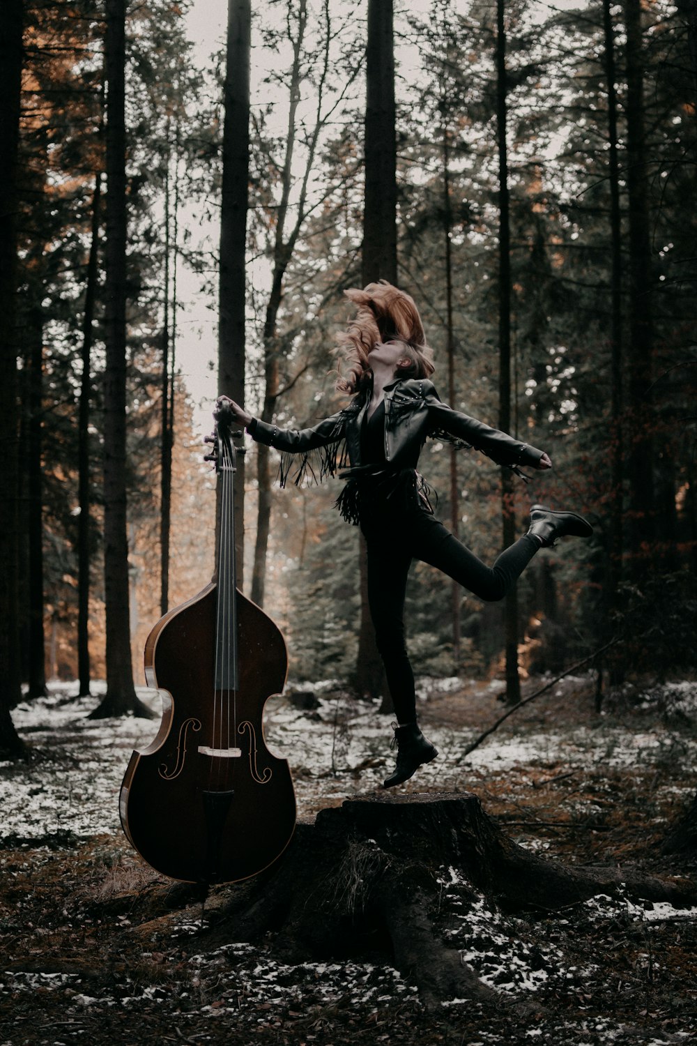 woman in black jacket and black pants playing violin in forest during daytime