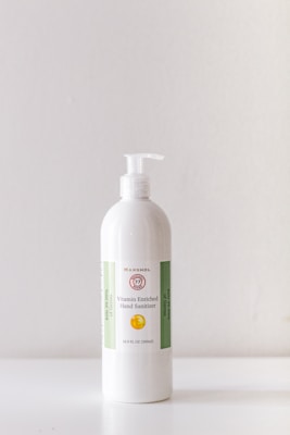 A white pump bottle labeled 'Vitamin Enriched Hand Sanitizer' with a green label bearing further text. The bottle sits on a plain white surface against a neutral background.