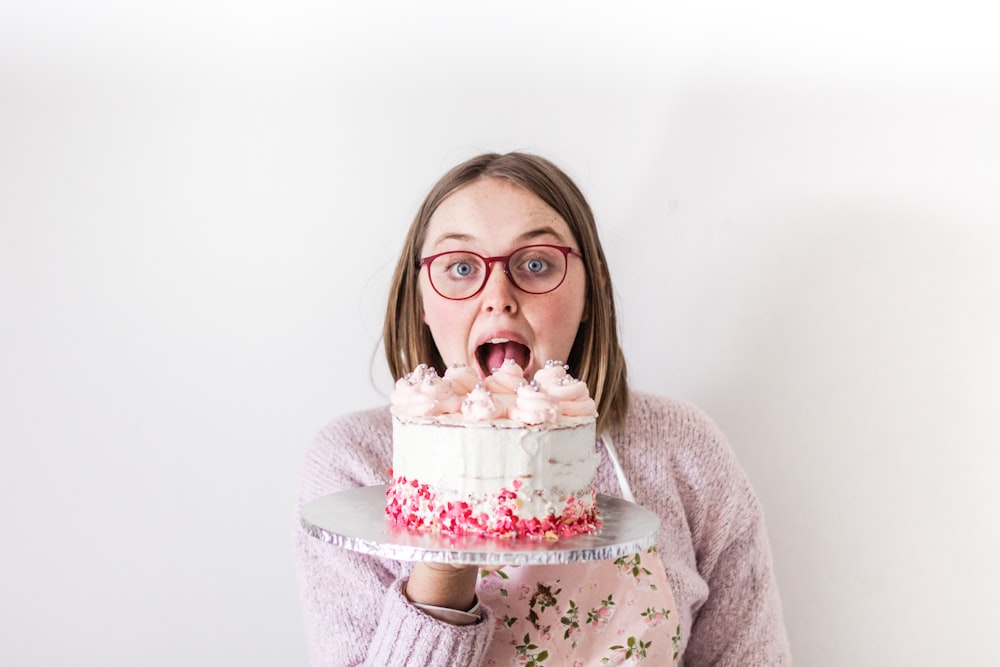 woman in gray sweater holding white and pink cake