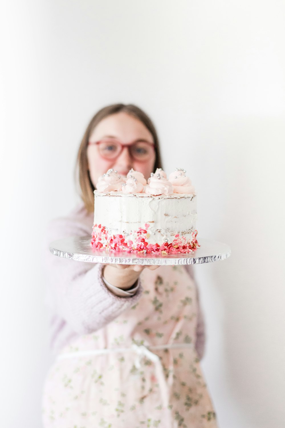 girl in white and pink sweater holding white and pink cake