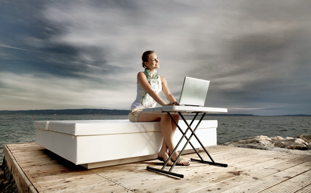 woman in white tank top sitting on white chair using macbook