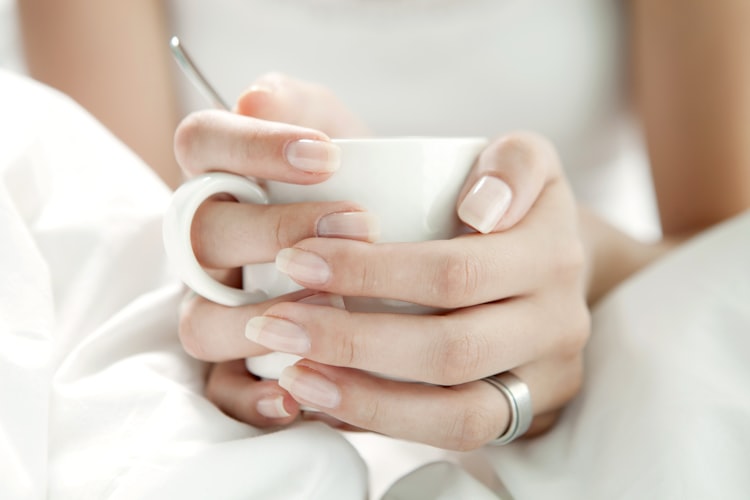 Mãos femininas com esmalte segurando uma xícara