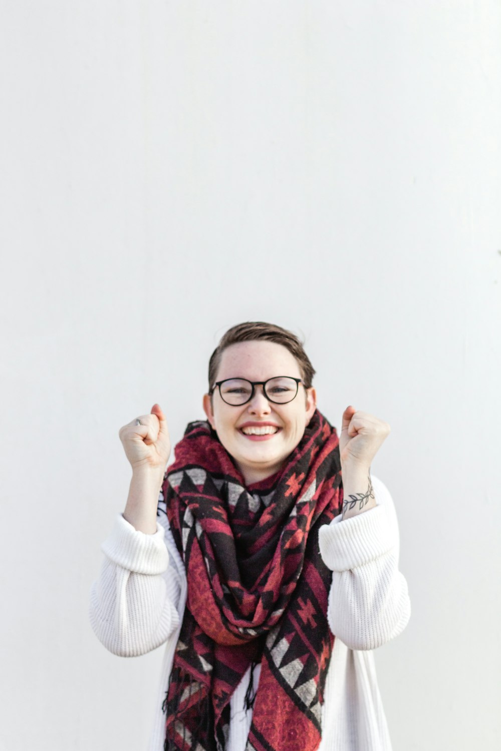 Femme en pull blanc portant une écharpe rouge et des lunettes à monture noire