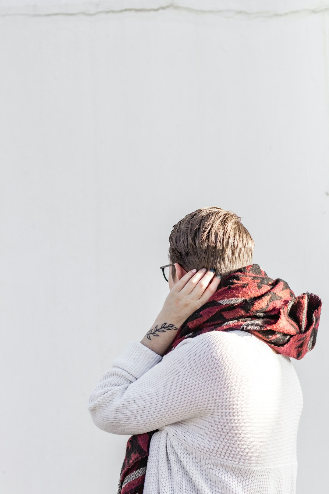 woman in white sweater covering her face with red and brown scarf