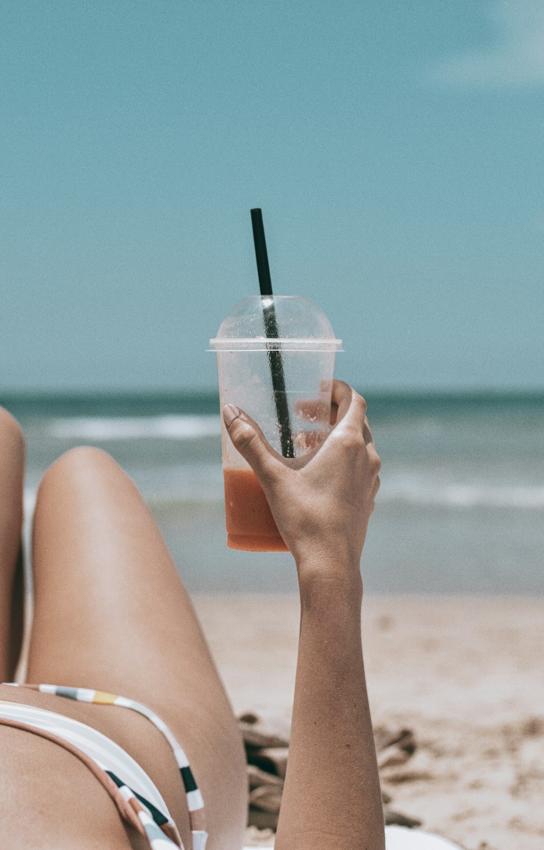 person holding clear plastic cup with green straw