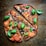 A delicious pizza with a thin crust, topped with tomato slices, pepperoni, black olives, fresh basil leaves, and melted cheese. The pizza is cut into large slices and sprinkled with herbs, set on a rustic wooden surface.