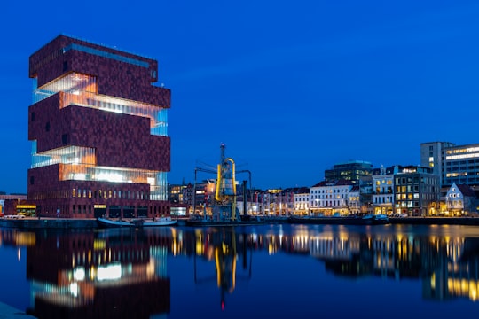 brown concrete building near body of water during night time in Museum aan de Stroom Belgium