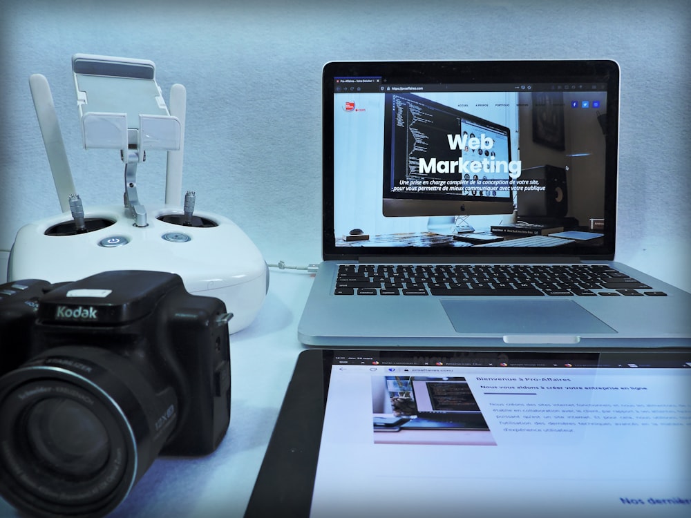 macbook pro beside black dslr camera on white table