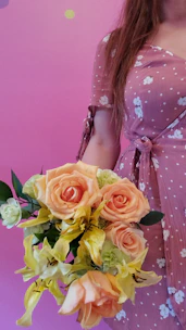 A woman in a soft pink dress smiling while holding a bouquet of fresh roses, with Valentine’s decorations in the background.