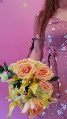 A woman in a soft pink dress smiling while holding a bouquet of fresh roses, with Valentine’s decorations in the background.
