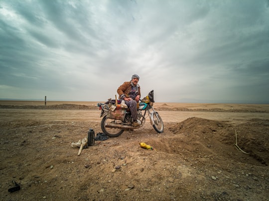 man in orange jacket riding on bicycle on brown sand during daytime in Ghom Iran