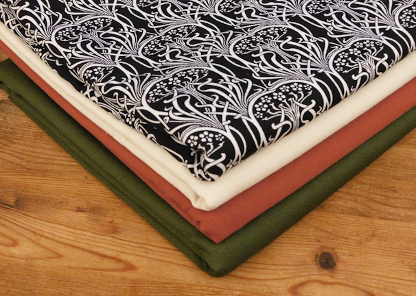 Close-up of a neatly folded black cotton dhoti with subtle gold border, resting on a warm cream fabric background.