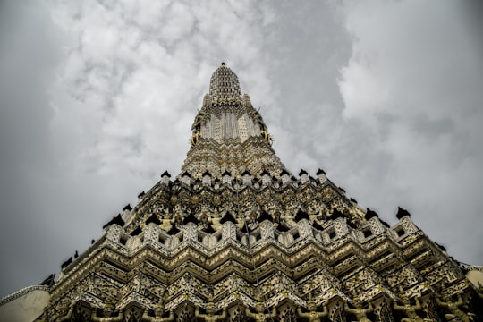 gold and white concrete building under white clouds in Wat Arun Ratchawararam Ratchawaramahawihan Thailand