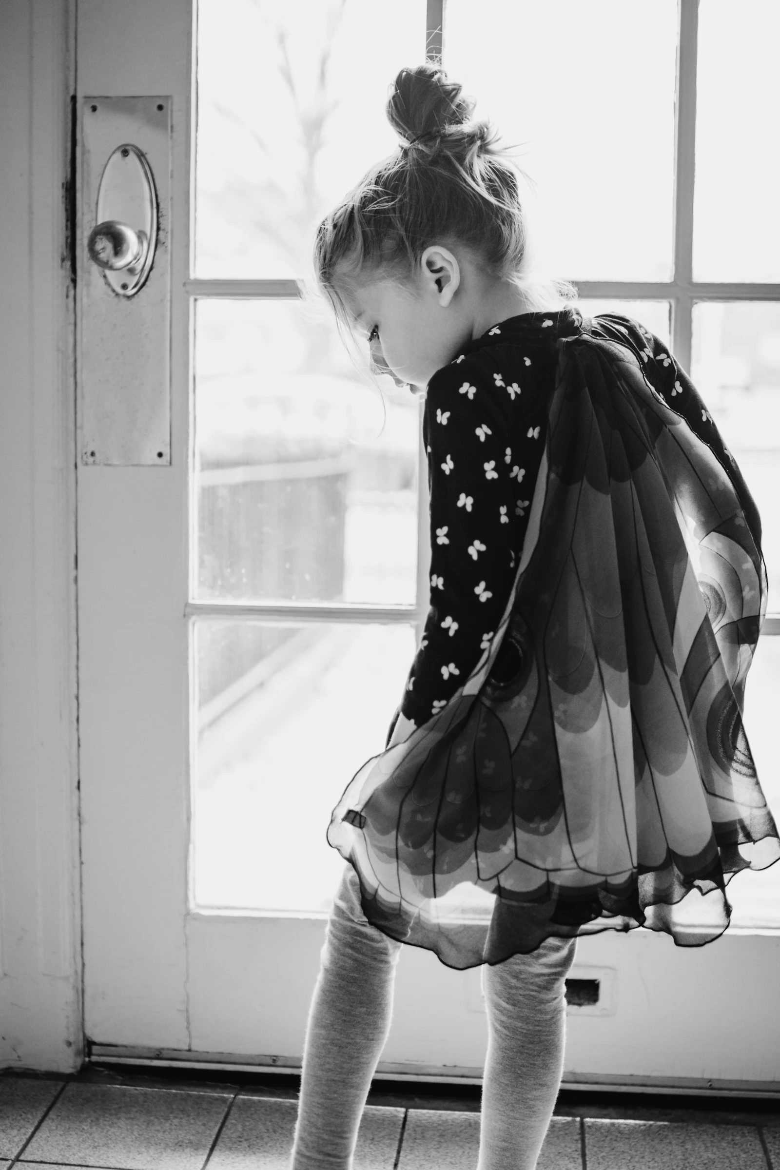 A child in a polka dot dress looks out a window in soft morning light