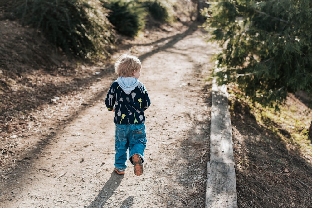 child in blue denim jacket standing on brown dirt road during daytime