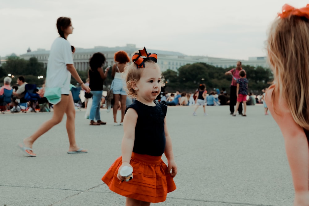 girl in black sleeveless dress and orange skirt standing on gray concrete floor during daytime