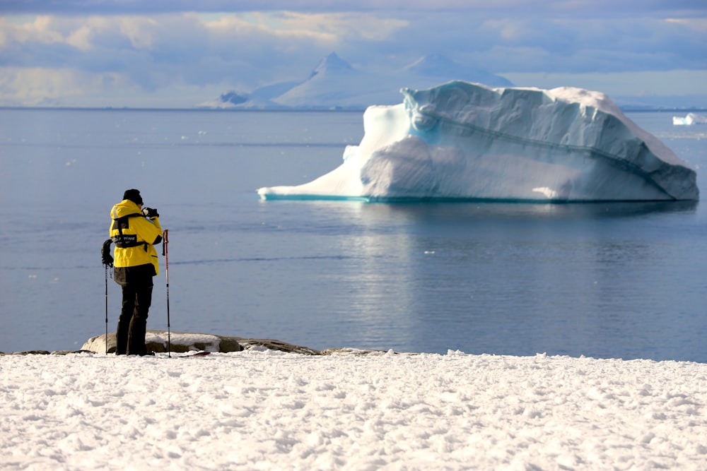 person in yellow jacket standing on white snow covered ground near body of water during daytime