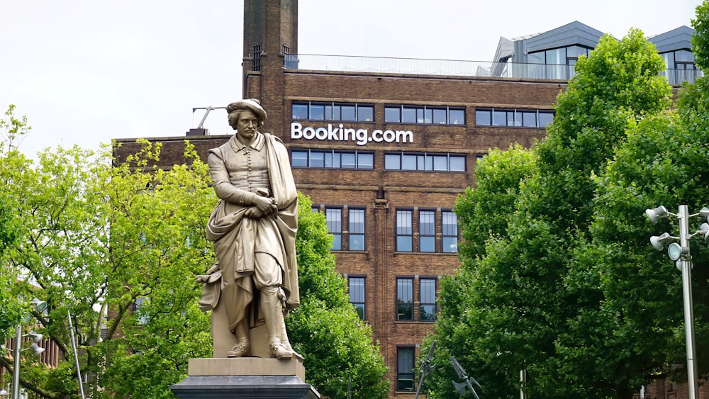 Statua dell'uomo che tiene il libro vicino all'edificio in cemento marrone durante il giorno
