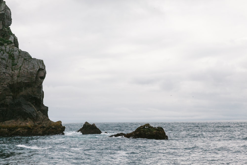 gray rock formation on sea under white clouds during daytime