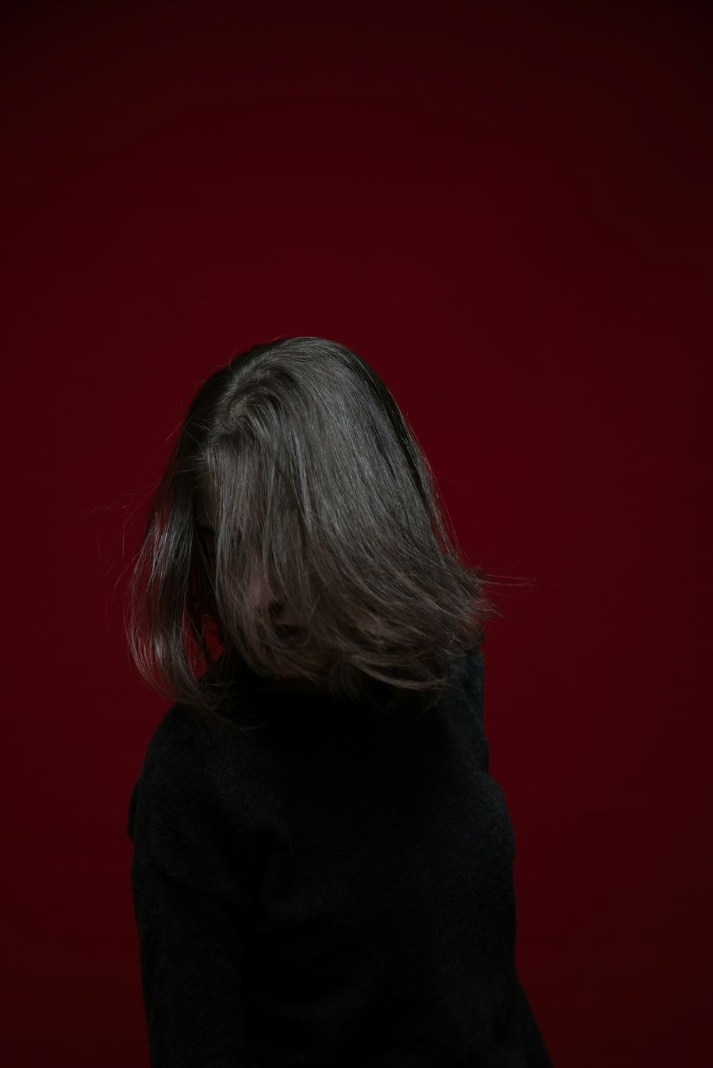 Mujer con sudadera con capucha negra de pie cerca de la pared roja