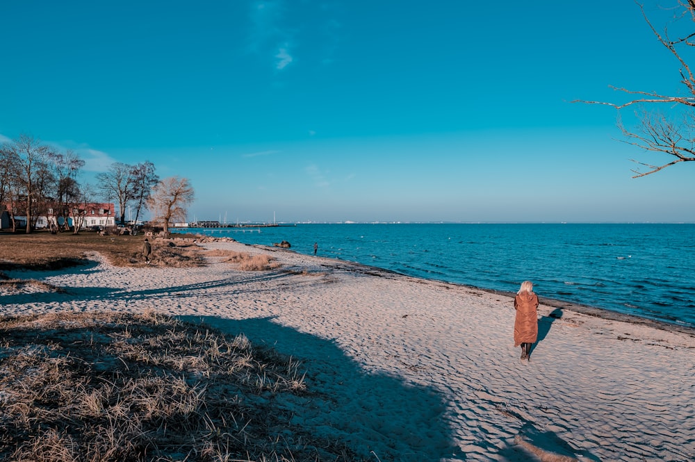 woman in brown jacket walking on seashore during daytime