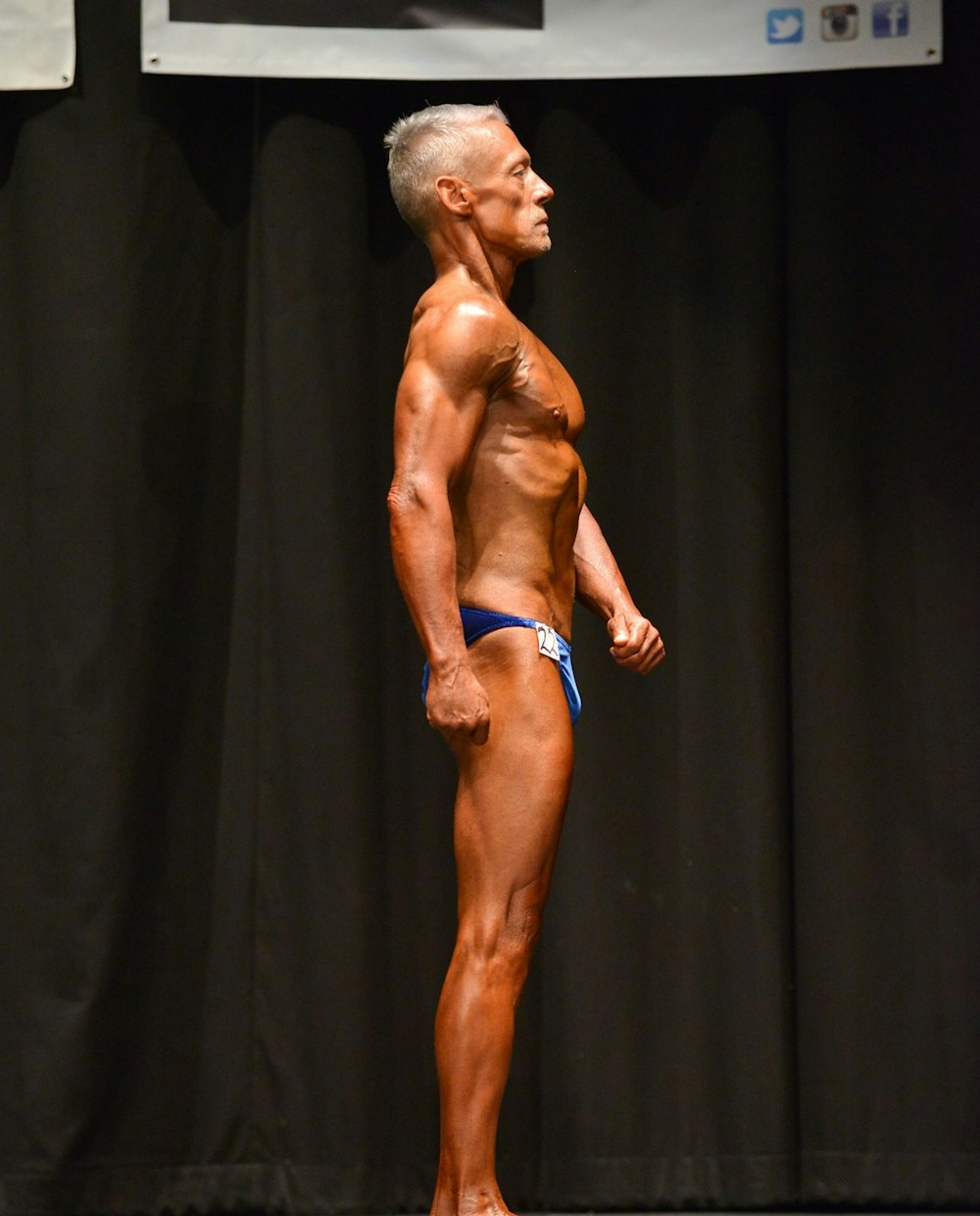 topless man in blue brief standing on black textile