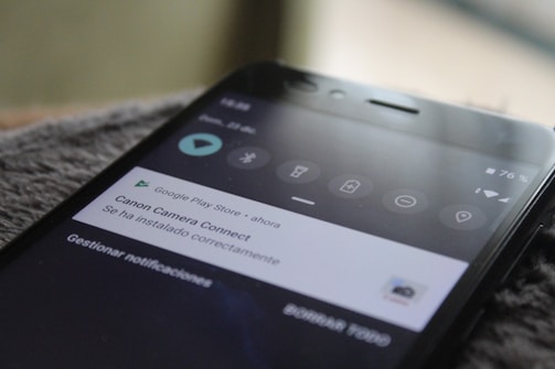 Close-up view of a smartphone screen displaying a notification from the Google Play Store, indicating that the Canon Camera Connect app has been successfully installed. The phone shows a 76% battery charge in the top right corner and several status icons.