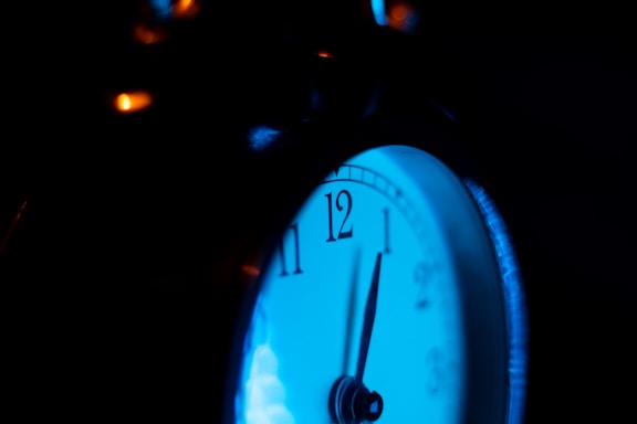 A close-up of a rugged industrial digital clock mounted on a factory wall, glowing brightly.
