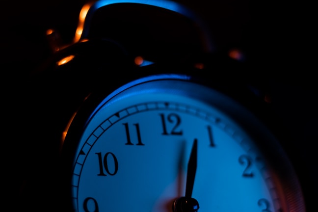 Close-up of a sleek red LED digital alarm clock glowing softly in a dark room.