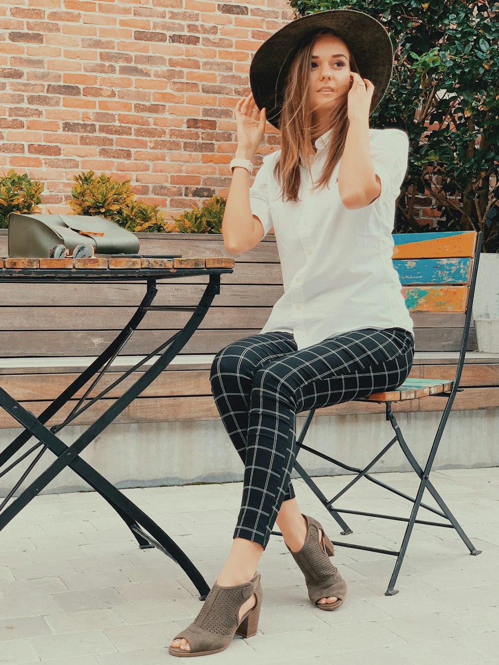 Mujer con camisa blanca y pantalones a cuadros blancos y negros sentada en una silla de metal negro