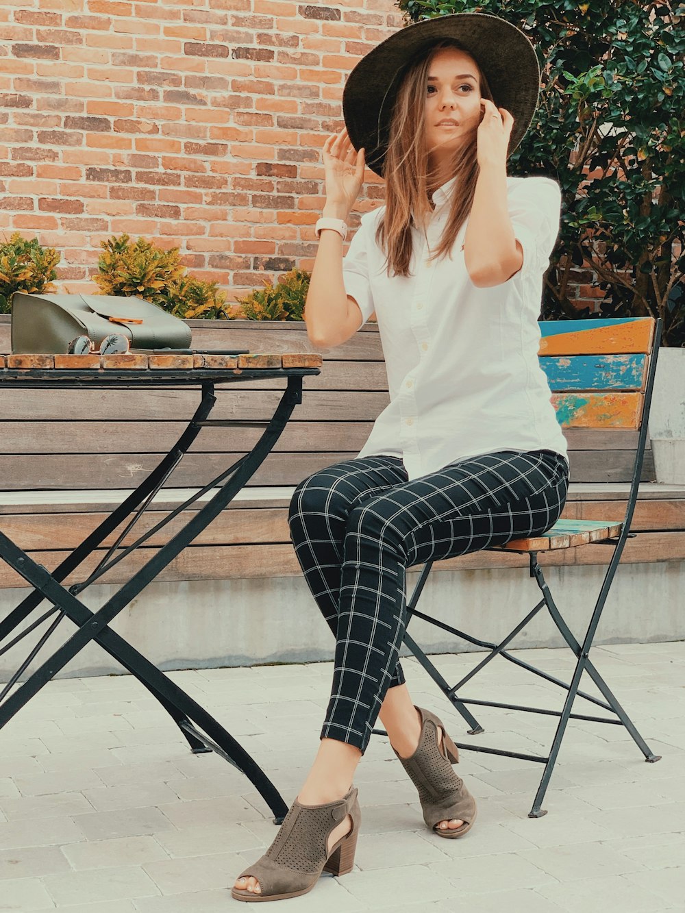woman in white shirt and black and white plaid pants sitting on black metal chair