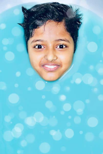 A cheerful swim instructor teaching a smiling child how to float in a bright, kid-friendly pool.