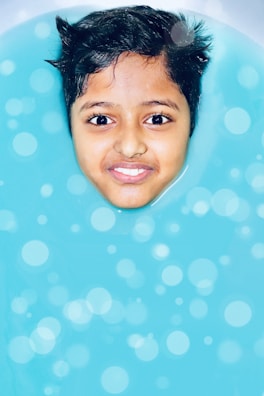 A smiling instructor helping a young child float on their back in a bright swimming pool.