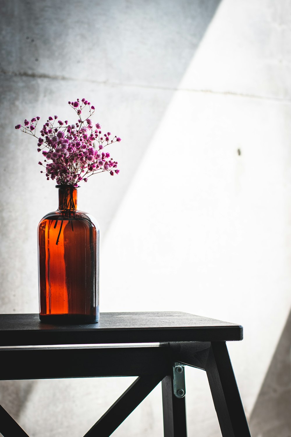 flores púrpuras en botella de vidrio marrón sobre mesa negra