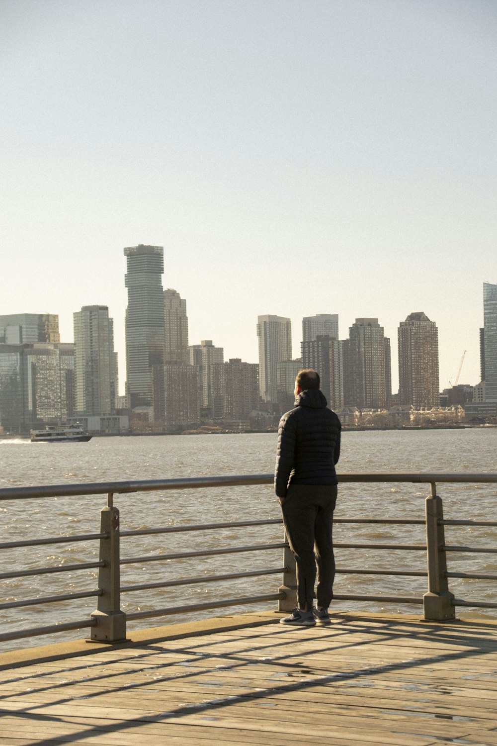 man in black jacket and black pants standing on brown wooden dock during daytime