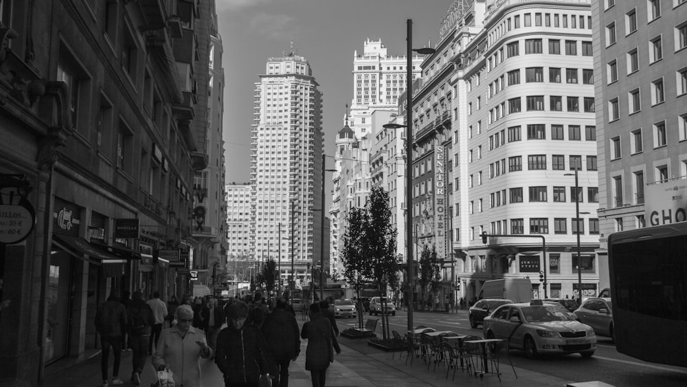 grayscale photo of people walking on street near high rise buildings