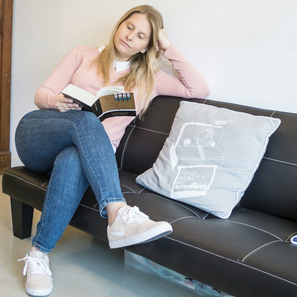 woman in pink long sleeve shirt and blue denim jeans sitting on black leather couch