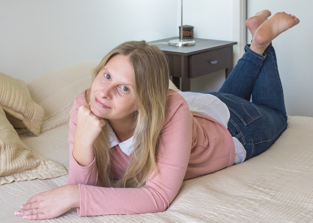 woman in pink long sleeve shirt and blue denim jeans lying on bed