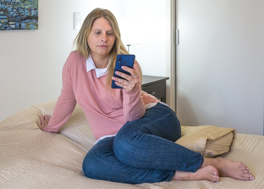woman in pink long sleeve shirt and blue denim jeans sitting on brown couch
