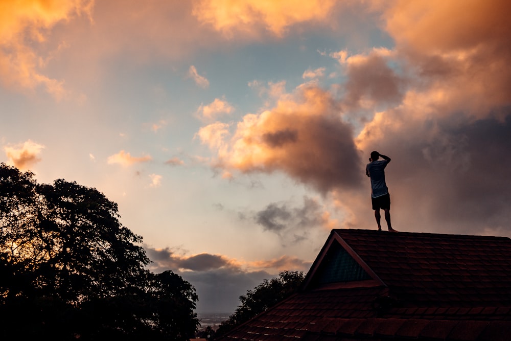Silueta de la persona de pie en el techo bajo el cielo nublado durante la puesta del sol