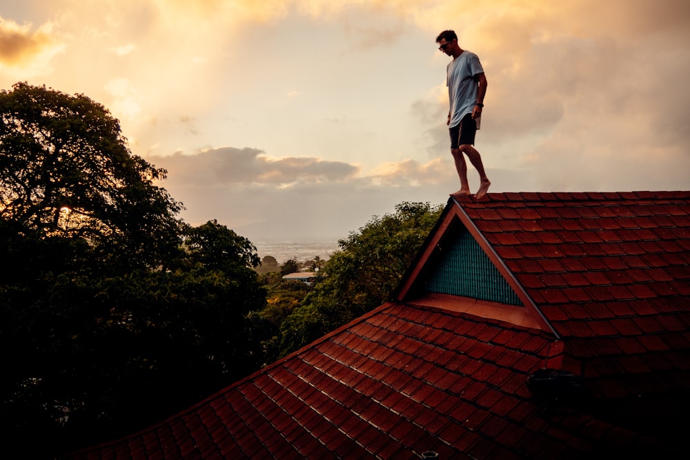 man in white shirt and gray pants standing on brown roof during daytime