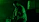 A silhouetted musician playing an electric guitar is bathed in green light. The background is dark, with a few indistinct shapes, possibly other band members or equipment.