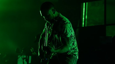 Guitarist shredding fiercely with gritty industrial backdrop and acid green accents.