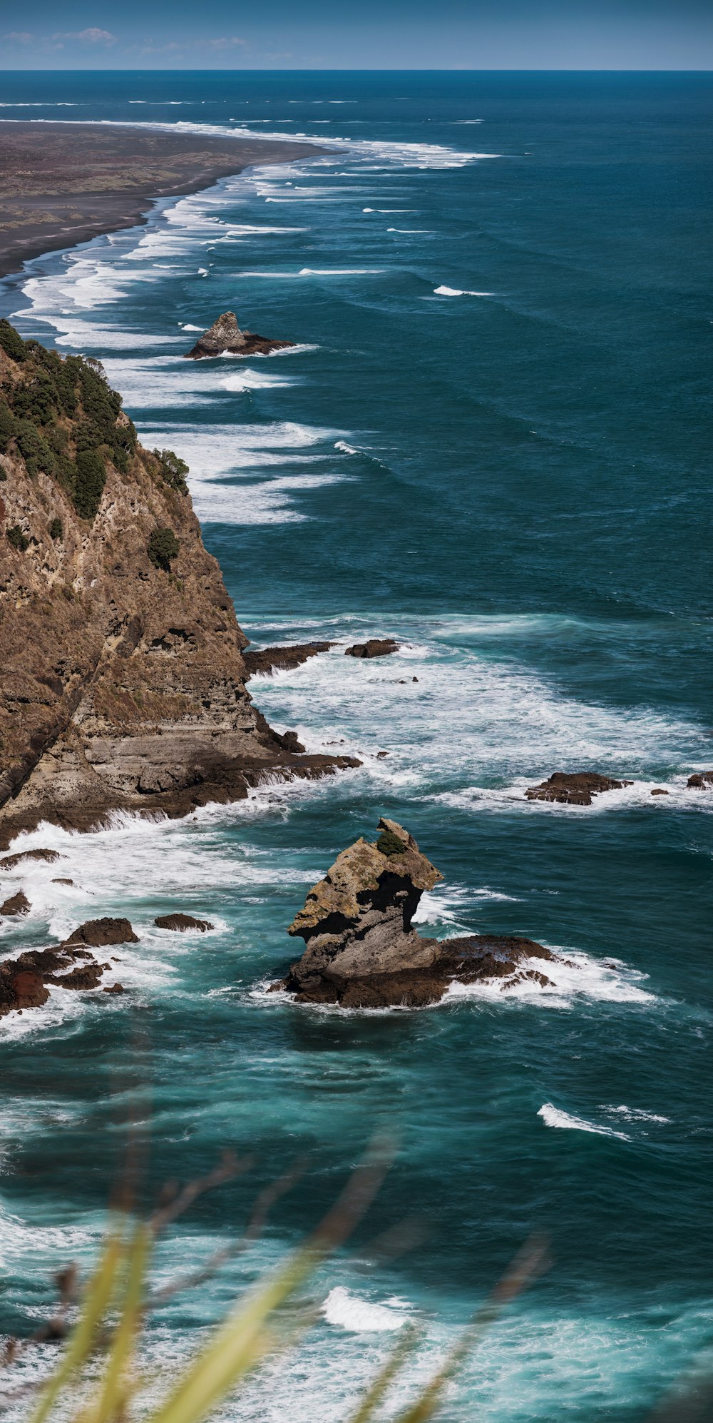 man in black shirt sitting on rock formation in front of sea during daytime